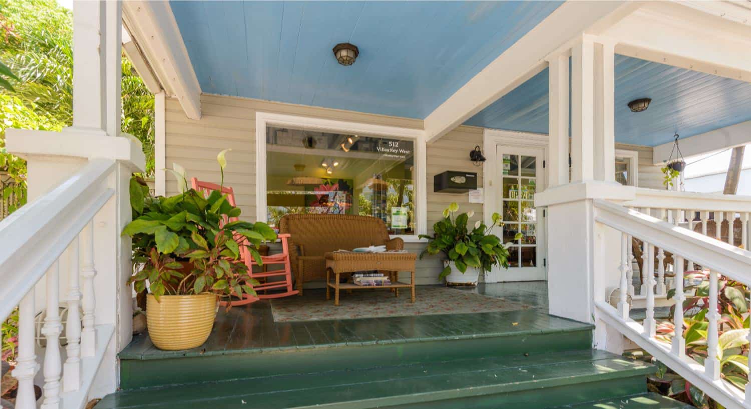 Front entrance of property with front porch, dark green wooden steps and flooring, wicker love seat, and salmon wooden rocking chair