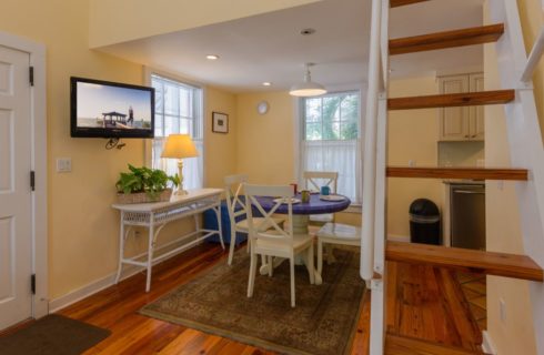Dining area with yellow walls, white trim, hardwood flooring, flat-screen tv, small table with blue top, and four white chairs