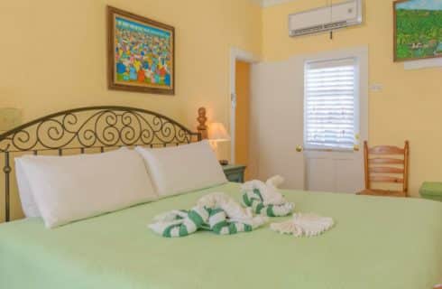 Bedroom with yellow walls, white trim, wooden bed, white linens, light green comforter, and two white and green frog-shaped towels on the bed