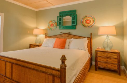 Bedroom with light green walls, hardwood flooring, brown wicker bed, white lines, and brown wicker nightstands