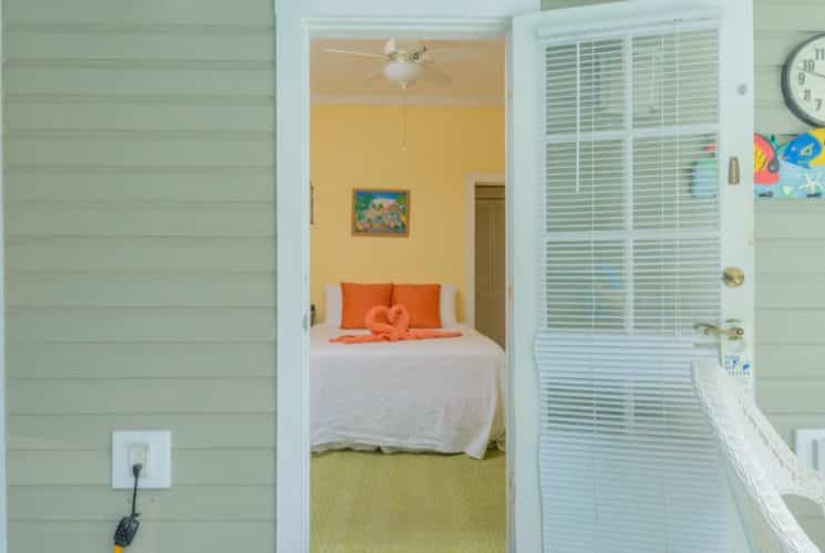 View into bedroom with yellow walls, white trim, bed with white linens and orange accent pillows, and two orange swan-shaped towels on the bed